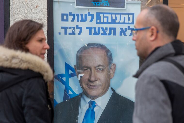 People look at a poster of Israel Prime Minister and governing Likud party leader Benjamin Netanyahu at a voting center in the northern Israeli city of Hadera on Thursday.