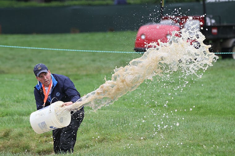 A Merion volunteer uses a five-gallon bucket to bail water out of a fairway bunker on the first hole after heavy rain on Monday morning. (Michael Bryant/Staff Photographer)