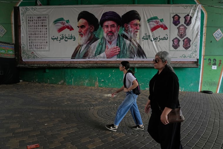 Women walk past a banner showing portraits of the late Iranian revolutionary founder Ayatollah Khomeini, left, Supreme Leader Ayatollah Mojtaba Khamenei, center, and the late Supreme Leader Ayatollah Ali Khamenei, who was killed in the U.S. and Israel strike on Feb. 28, under a bridge in northern Tehran, Iran, Sunday, Aug. 2, 2026.