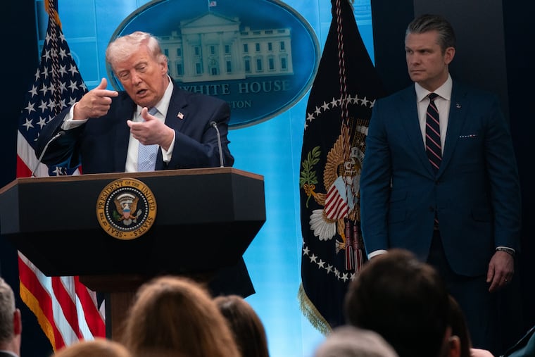 President Donald Trump appears to mimic firing a rifle while speaking to reporters at the White House on Monday, standing next to Defense Secretary Pete Hegseth.