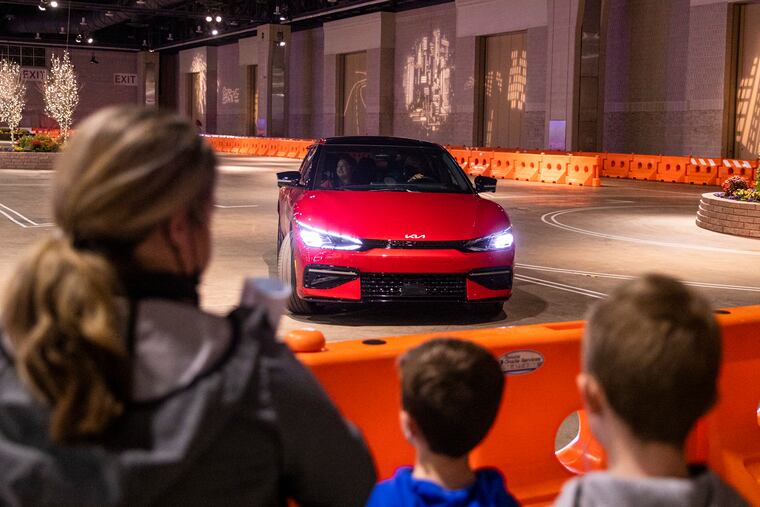 Danielle O’Brien, of Barnegat, N.J., and her children Declan O’Brien, 7, and Finn O’Brien, 9, watch the test drive for the 2022 Kia EV6 at the Philadelphia Auto Show.