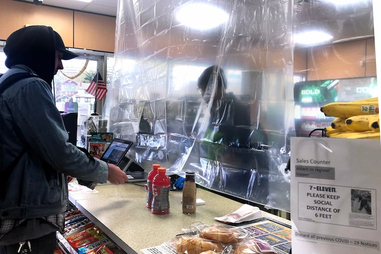 Workers behind the counter at the 7-11 on the White Horse Pike in Oaklyn are protected from customers and social distancing by a clear shower curtain March 31, 2020, as New Jersey’s shutdown of schools and nonessential businesses because of the coronavirus pandemic continues.