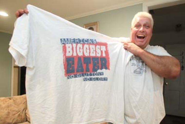 El Wingador, who in real life is retired 50-year-old truck driver Bill Simmons (CQ - HE WAS ALSO CALLED BOB ON THE PHOTO ASSIGNMENT BUT IT IS BILL) from Woodbury Heights, has now retired also from competitive eating, after being a five-time WIng Bowl champ. He is trying to sell a reality show, "America's Biggest Eater", in which he would be an adviser to gluttonous competitive eaters. He holds up a 4XL T-shirt that is even too big for him. ( Charles Fox / Staff Photographer ) JWING23P, 2/16/2012, BILL SIMMONS (CQ), 334 IVY DRIVE, WOODBURY HEIGHTS, NJ