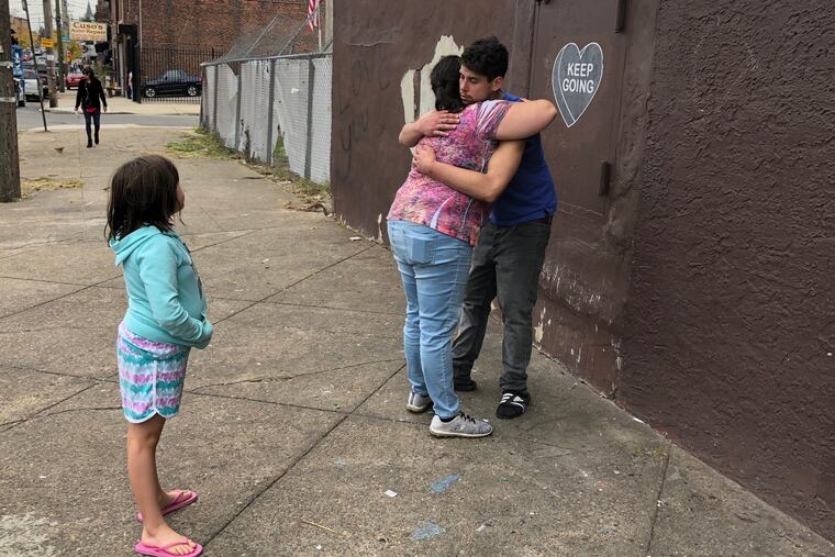 As her daughter Sarah, 8, looks on, Meredith Redmond, center, hugs her oldest daughter Rhiannon's boyfriend, at a memorial for the 22-year-old on Kensington Avenue.