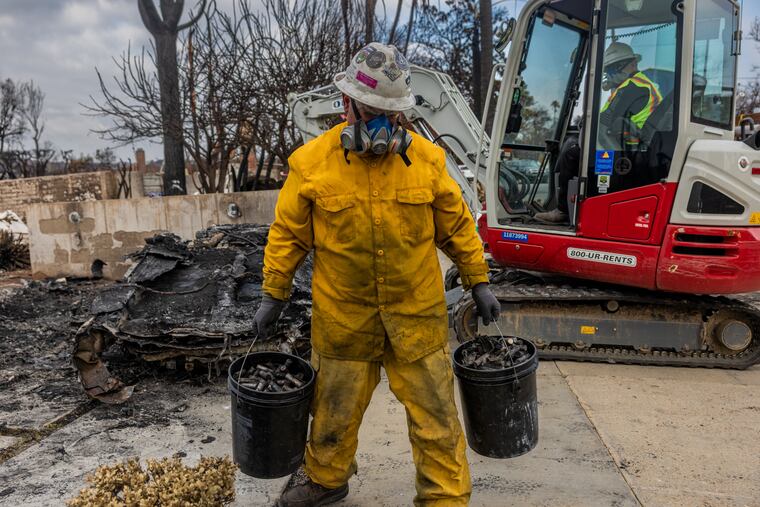 A worker with the U.S. Environmental Protection Agency holds buckets of burned lithium-ion batteries removed from a burned electric vehicle (EV) after the Palisades Fire in Los Angeles, Calif., on Thursday, Jan. 30, 2025.