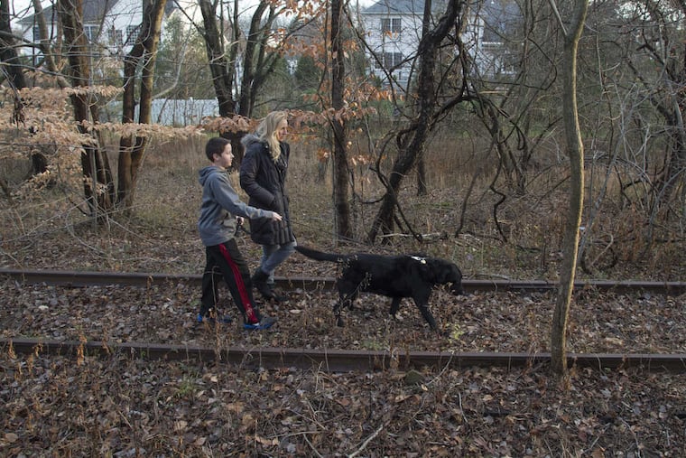 Brig Masone, 50, and her son Dominic, 12, walk their dog Lucky along the old SEPTA Newtown rail line tracks behind their Churchville development.