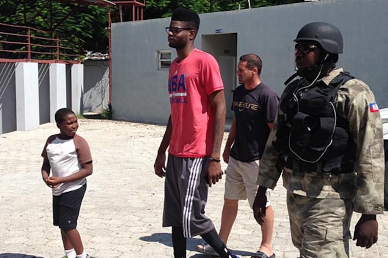 A little Haitian onlooker walks beside Nerlens Noel as he prepares to enter Gymnasium Vincent with manager Chris Driscoll and Port-au-Prince police officer Ricot "Mutombo" St. Louis. (Keith Pompey/Staff)