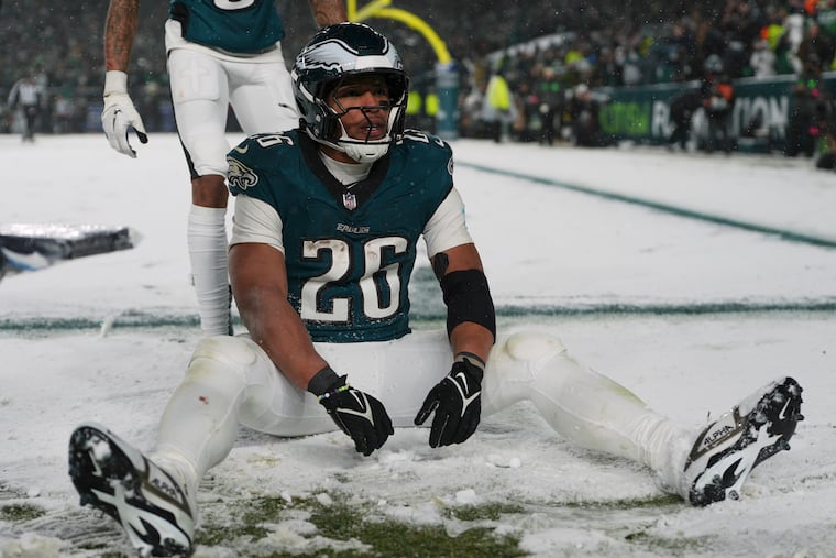 Saquon Barkley (26) sits in the snow as he celebrates his touchdown during the second half of an NFC divisional playoff game against the Los Angeles Rams on Sunday, Jan. 19, 2025.