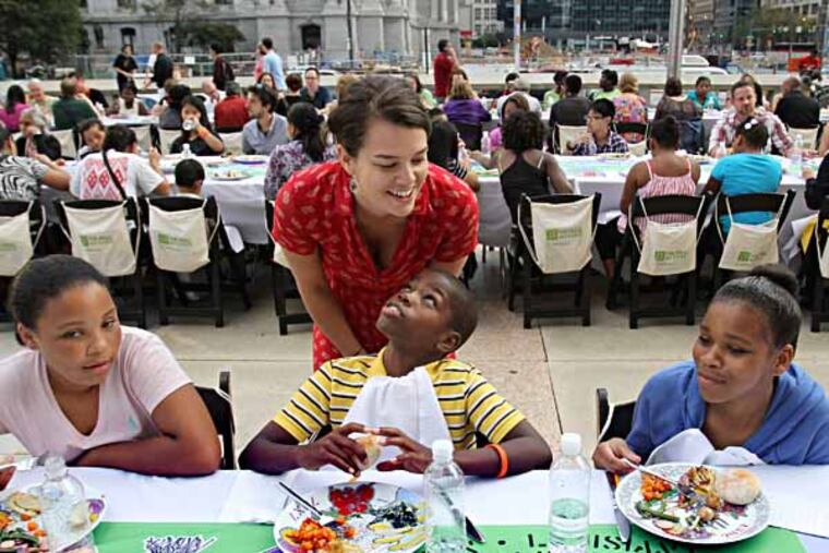 Sarah Folger (center), a Mural Arts educator, checks on art students from left, Mattie Bullock, Samear McCaskill, and Danielle Faison as they dine. fromThe City of Philadelphia Mural Arts Program culminates an 18-month project with internationally-renowned Paris-based artists Lucy + Jorge Orta with a free meal for 900 guests with the backdrop of Philadelphia’s City Hall. An unusual event of public art, 70x7 The Meal, act XXXIV, is a collaboration between the Mural Arts Program and the Ortas. This visual and performance art piece gathers people around a 904-foot communal table to engage in conversation about the issues of heirloom foods and their role in creating a healthier food system for people and the environment. Saturday, October 5, 2013. ( MICHAEL S. WIRTZ / Staff )