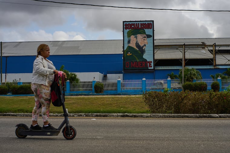 A woman rides an electric scooter past a factory displaying an image depicting the late Cuban leader Fidel Castro, bearing the words "Socialism or Death", in Havana on Thursday.