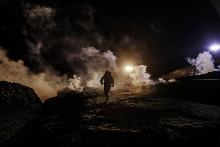 Migrants run as tear gas is thrown by U.S. Border Protection officers to the Mexican side of the border fence after they climbed the fence to get to San Diego, Calif., from Tijuana, Mexico, Tuesday, Jan. 1, 2019.