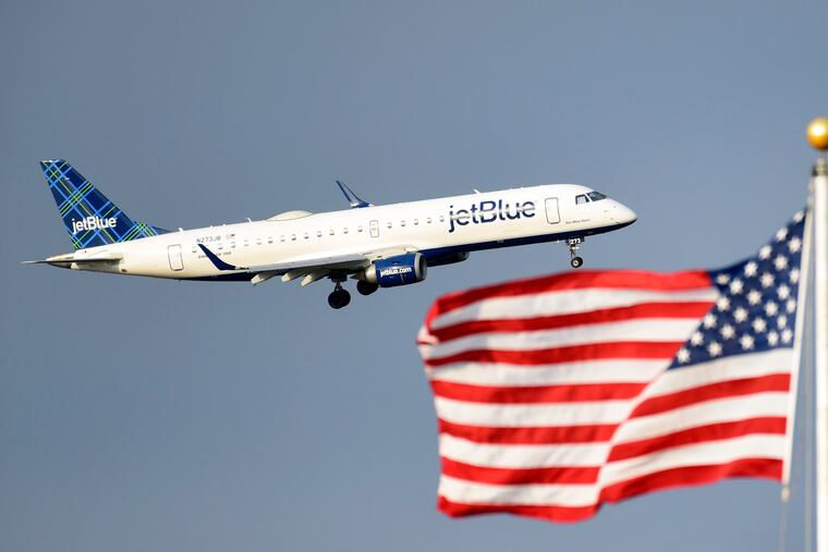 FILE - In this Sept. 21, 2018, file photo, a plane flies past the American flag in Washington. JetBlue plans to join bigger rivals in offering flights between the U.S. and Europe, starting with London in 2021.