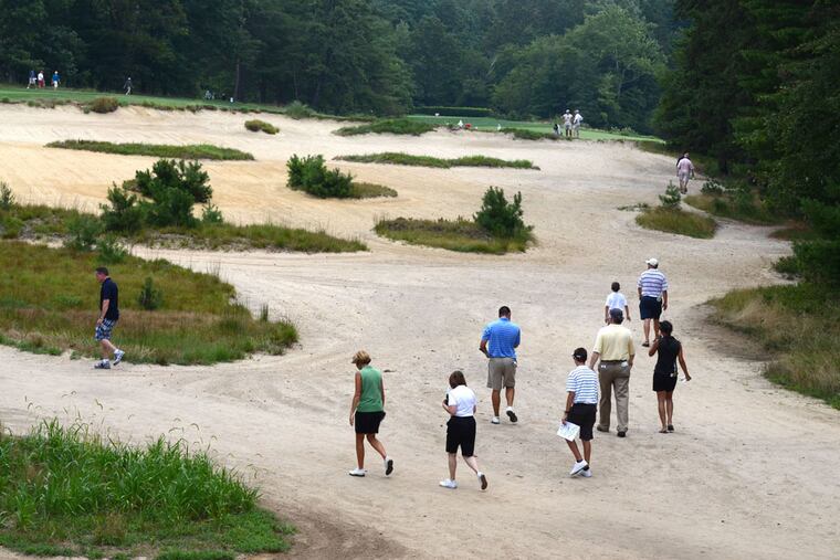 Spectators walk through a huge waste bunker on the 16th hole at famed Pine Valley Golf Club.
