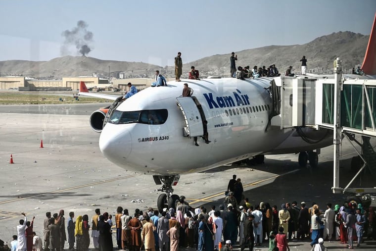 Afghan people climb atop a plane as they wait at the Kabul airport in Kabul on August 16, 2021, after a stunningly swift end to Afghanistan's 20-year war, as thousands of people mobbed the city's airport trying to flee the group's feared hardline brand of Islamist rule.