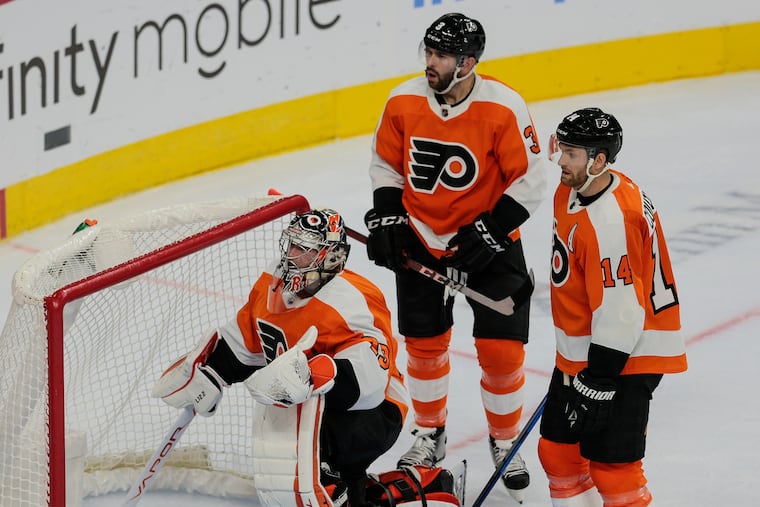 Flyers goalie Carter Hart takes the puck from the net after Vancouver's Alex Chiasson scored in the second period. Defenseman Keith Yandle and center Sean Couturier look on.