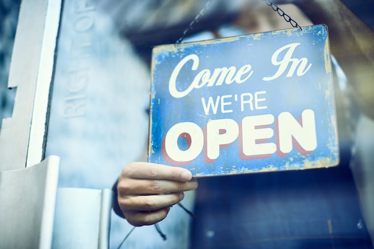 In this stock photo, a small-business employee hangs a sign in the window to tell customers the business is open.
