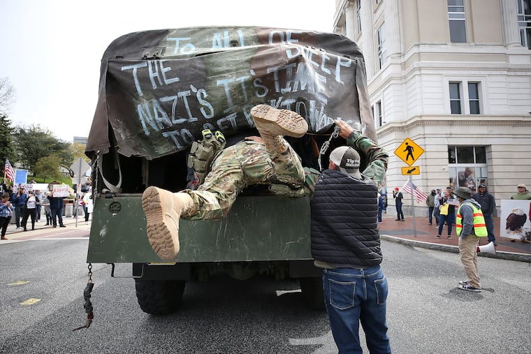 A militia member dives into the back of a truck after a protest outside the Capitol Complex in Harrisburg on April 20, 2020. They are calling for Gov. Tom Wolf to reopen the state's economy during the coronavirus outbreak.