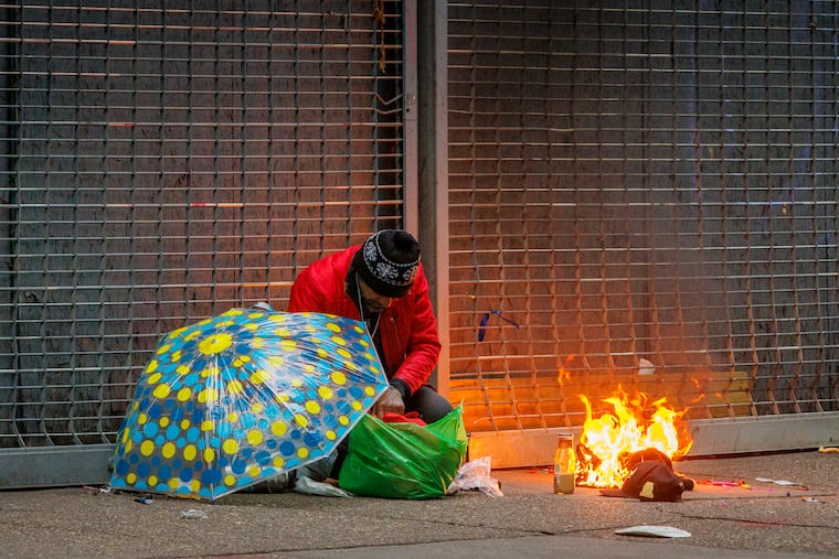 A man experiencing homelessness crouches next to a fire on the sidewalk of Kensington Avenue in April 2023. The city has launched a task force to walk through the area at night and extinguish open fires because of the risks of rogue flames.