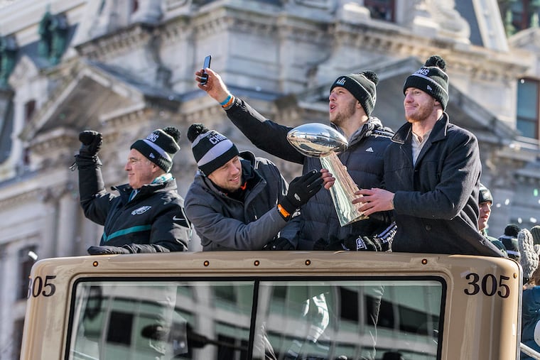 With City Hall in the background, Eagles quarterbacks (from left) Nick Foles, Nate Sudfeld and Carson Wentz show off the Vince Lombardi Trophy aboard their bus. At left is Eagles owner Jeffrey Lurie. MICHAEL BRYANT / Staff Photographer