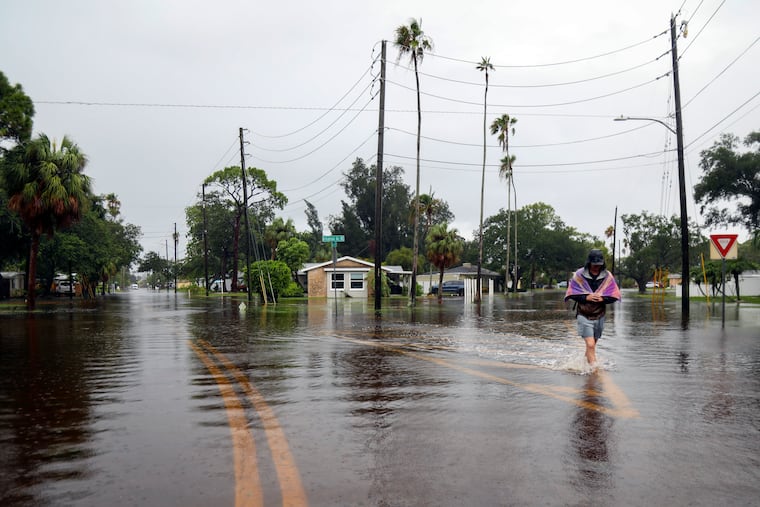 Carter Grooms, 25, of Tampa, Fla., wades through the streets in the Shore Acres neighborhood of St. Petersburg on Monday. Debby may bring heavy rains to the Philly region.