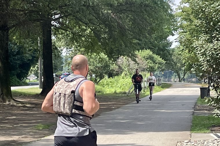 A runner and scooter riders utilize the walkway along Kelly Drive Sunday morning, not far from the parking lot where police early Saturday found the body of a man who had been fatally shot in the head.