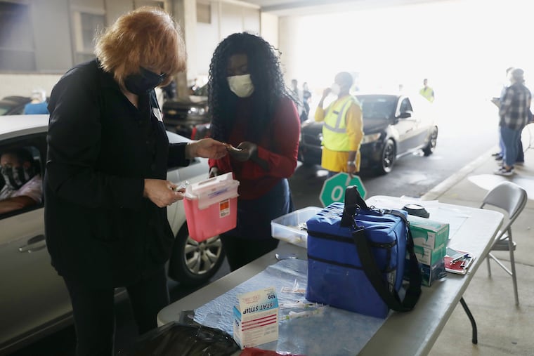 Volunteer Kathy Sullivan (left), a retired nurse, prepares to administer a flu shot as fellow volunteer Albertina Coleman, a pharmacy student, holds a sharps disposal container during a drive-through clinic for police officers and their family members at the Delaware Valley Intelligence Center in South Philadelphia on Wednesday, Oct. 21, 2020.