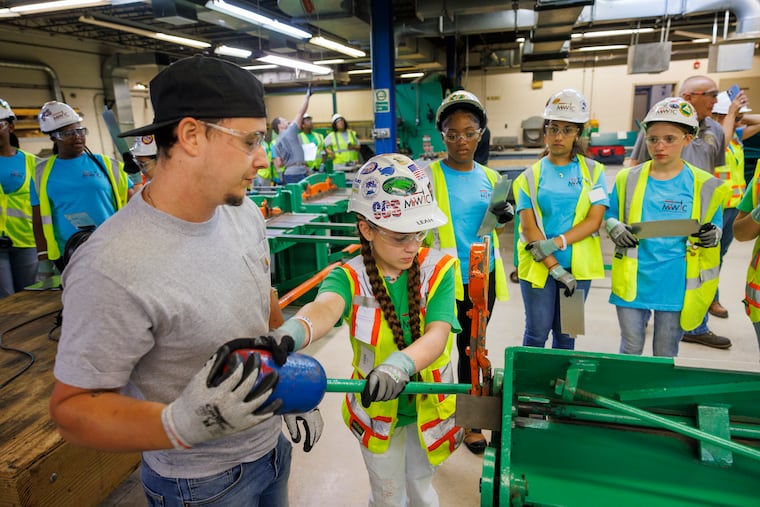 An apprentice at the Sheet Metal Workers’ Training Center of Local Union 19 in South Philadelphia helps a camper bend a sheet of metal during a workshop.