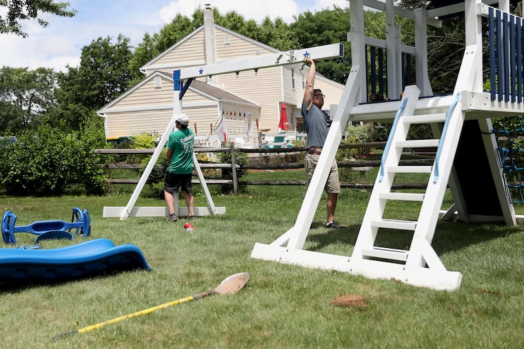 Elite Outdoor Structures co-owner Steve Moffitt (right) and installer Billy Feeley assemble a playset behind a customer's home in Lansdale on July 1. The coronavirus pandemic has increased demand for outdoor playsets, which are selling out quickly.