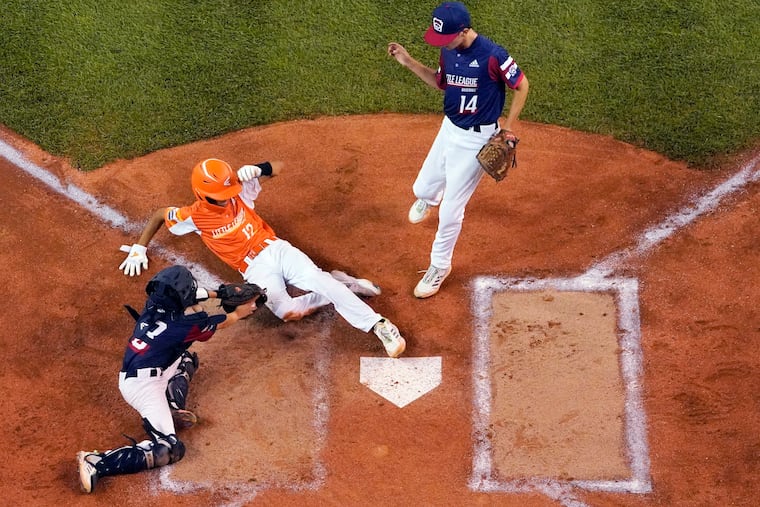 Lafayette, La.'s Nick Brown (12) scores past the tag attempt by Oaks, Pa. catcher Sean Kenney (8) on a wild pitch by starting pitcher Sam Buckley (14) during the first inning at the Little League World Series in South Williamsport, Pa., Saturday, Aug. 21, 2021. Louisiana won, 5-3.