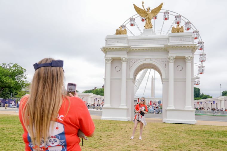 Visitors take photos at the Great American State Fair on the National Mall, with the ferris wheel and a model of the triumphal arch in the background, Thursday, July 9, 2026, in Washington. The proposed arch would be 250 feet tall.