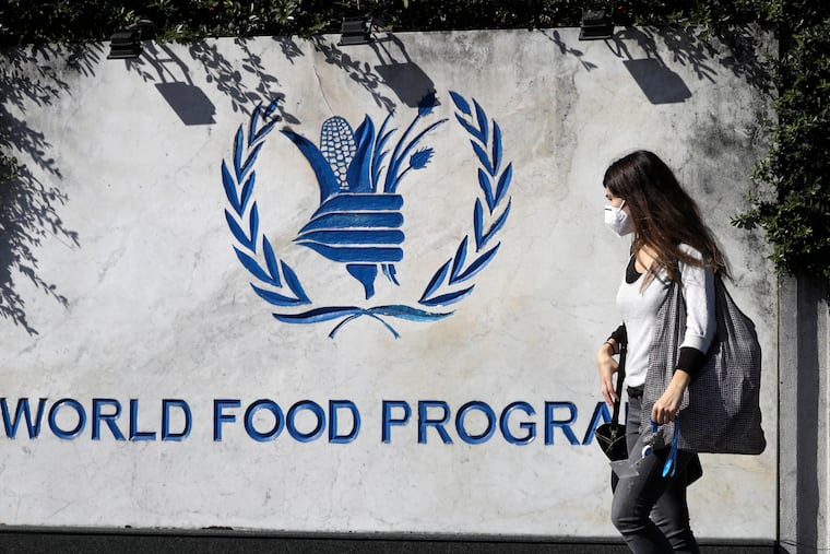 A woman wearing a face mask walks past a sign at the entrance of the United Nations World Food Program (WFP), in Rome on Oct. 9, 2020, after the WFP won the 2020 Nobel Peace Prize.