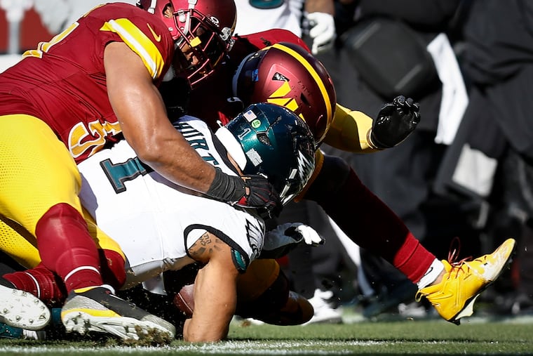 Eagles quarterback Jalen Hurts is tackled by Washington's Bobby Wagner and Frankie Luvu. Hurts left the game after this play.