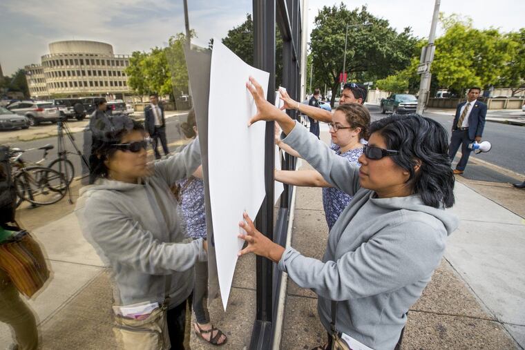 Catalina Perez and others stand with their signs pressed up against the windows at a U.S. Immigration and Customs Enforcement office in Philadelphia.