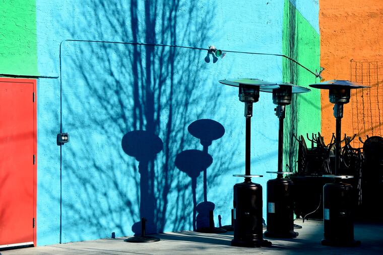 Space heaters and outdoor dining furniture are joined by the shadow of a winter-bare tree, a cold still life along East Passyunk Avenue.