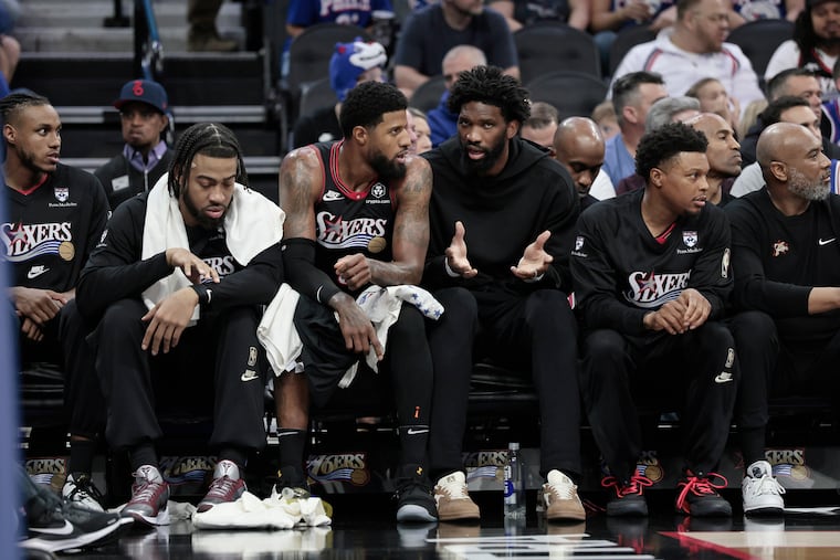 The Sixers' Paul George and Joel Embiid talk on the bench during the first half of an NBA play-in tournament basketball game.