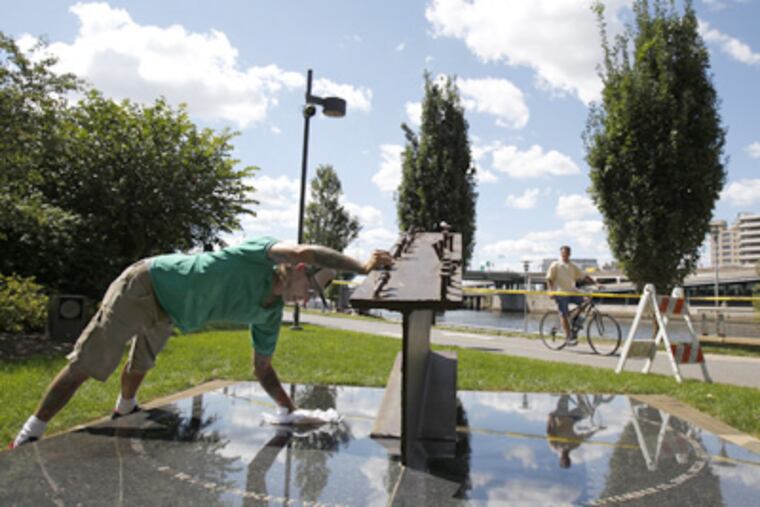 Eric Pauly cleans the memorial, which has the names of the three Philadelphia residents who died in the World Trade Center on 9/11. (David Maialetti / Staff Photographer)