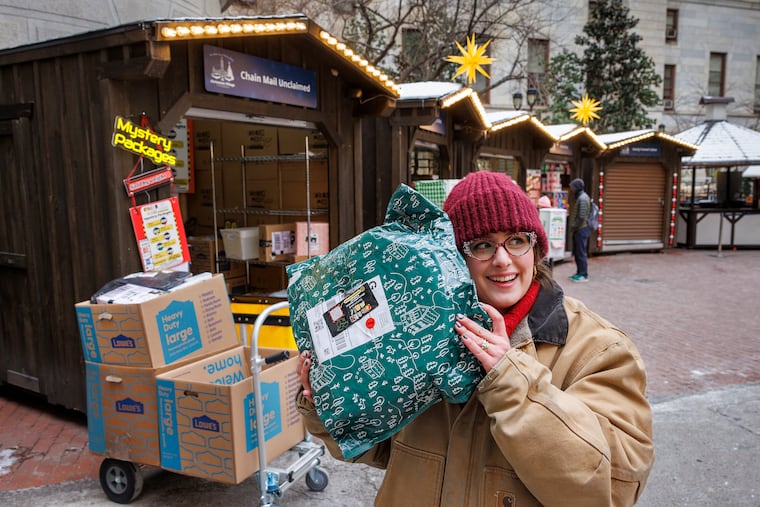Emma Zielinski, owner of Chain Mail Unclaimed, gives a package a shake. Her business is selling unclaimed packages to shoppers looking for a surprise gift at the Christmas Village in the interior courtyard of City Hall.