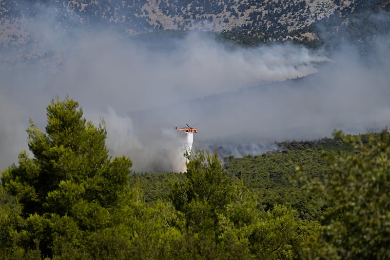 A firefighting helicopter drops water over a smoke-filled forest during a wildfire near Porto Germeno, northwest of Athens, Greece, Sunday, Aug. 2, 2026. A collision between two helicopters Sunday left two crew members dead.