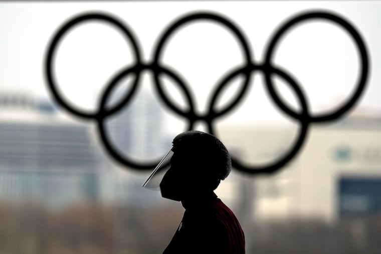 A person wearing a face shield walks past the Olympic rings inside the main media center at the 2022 Winter Olympics, Wednesday, Jan. 19, 2022, in Beijing. (AP Photo/David J. Phillip)
