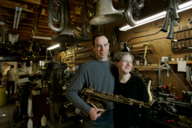 Bret Gustafson and his wife, Nadja, in their Roxborough instrument-repair shop. "Bret's a really, really good repairman," says Nadja, a jewelry-maker. "But he doesn't like charging people." They're moving to Australia, where someone else will handle the business end.