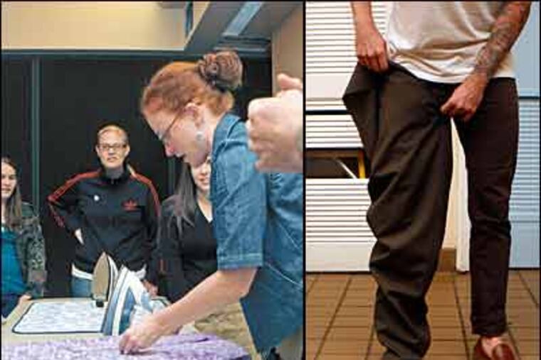 Megan Haupt illustrates sewing techniques for making a pair of draw-string pants. At right, Keegan O'Brien tries on one leg of a pair of pants he is making.(Bonnie Weller / Inquirer)