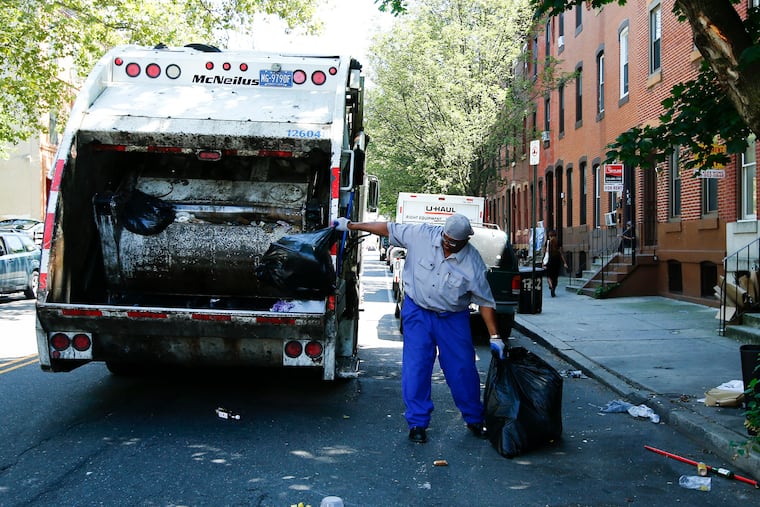 A City of Philadelphia sanitation worker prepares to toss trash into a garbage truck along the 1700 block of Diamond Street near the Temple University campus earlier this month.