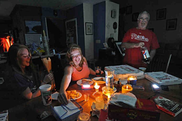 Laura (left), Emily, and Jim Cahill eat pizza by candlelight. Their Havertown home has not had power since Saturday. (April Saul/Staff)