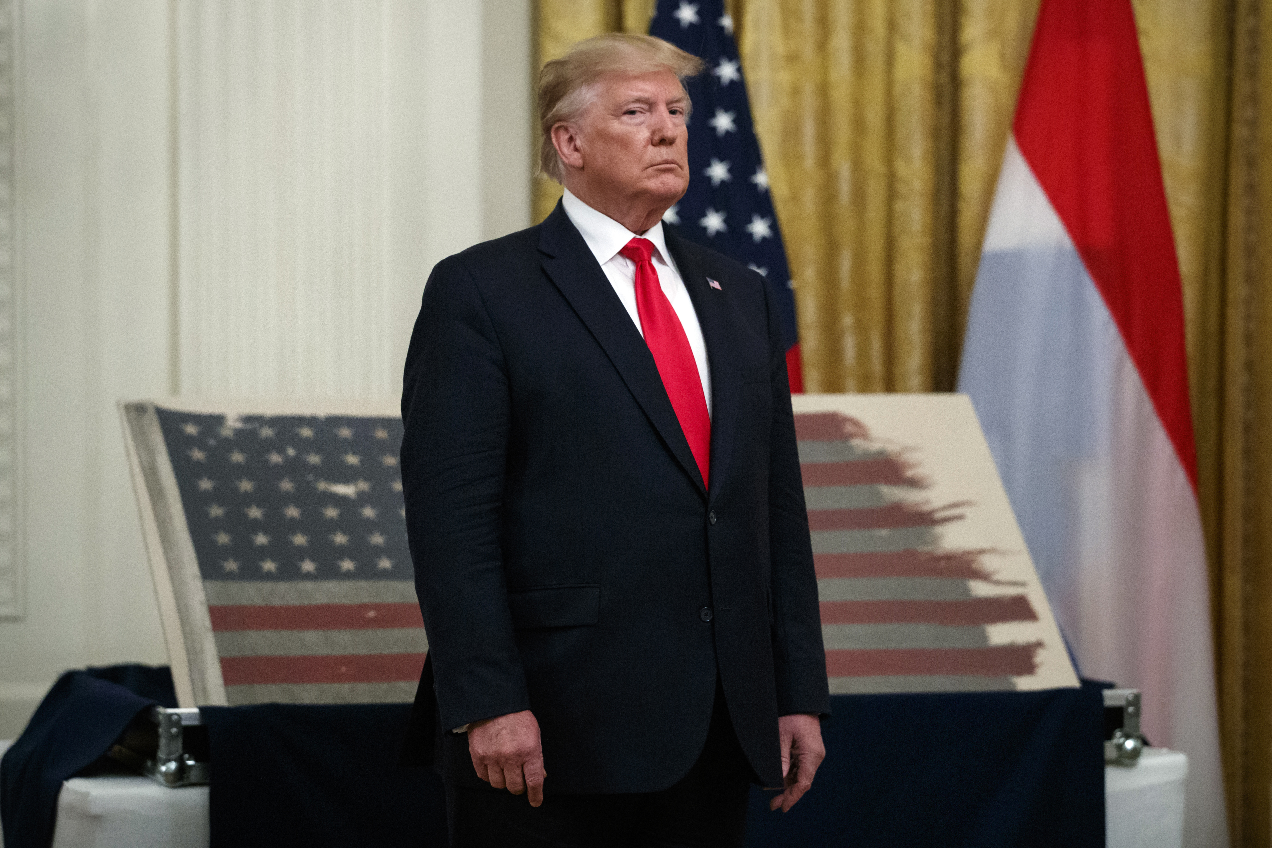 President Donald Trump stands in front of a 48-star flag flown on a U.S. Naval vessel during the D-Day invasion during a ceremony in the East Room of the White House.