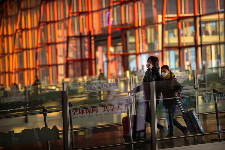 Travelers wearing face masks walk along a concourse at Beijing Capital International Airport in China.