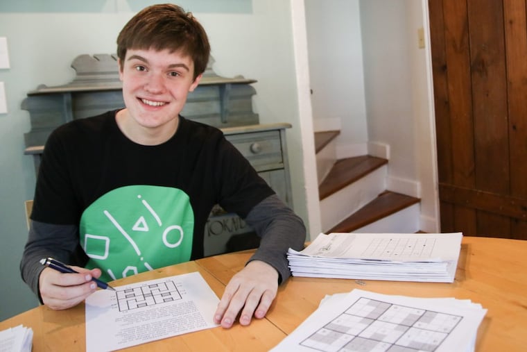 Walker Anderson poses for a photo surrounded by piles of puzzles he has worked on recently.
