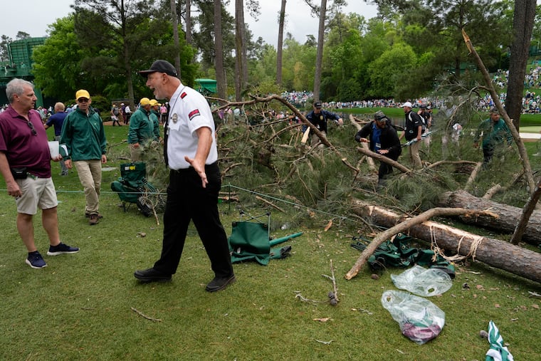 A security guard moves patrons away from trees that blew over on the 17th hole during the second round of the Masters on Friday.