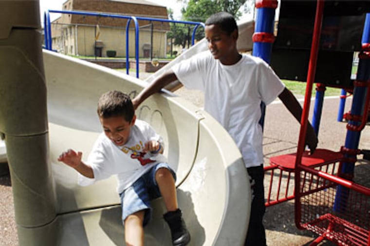 Above, Fernando Garcia sends his brother, Marcus, 3, down a slide at Whitman Park's little-used playground. (Sarah J. Glover / Inquirer)