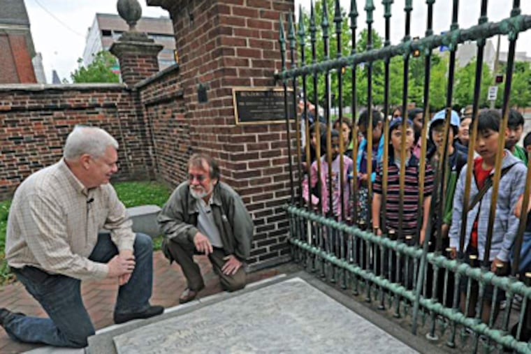 Authors Joe Farrell (left) and Joe Farley visit Benjamin Franklin's grave at the Christ Church Burial Ground as a group of touring schoolchildren look on. Franklin, who died in 1790, opted for a roughly hewn, flat gravestone rather than a grand mausoleum. APRIL SAUL / Staff Photographer