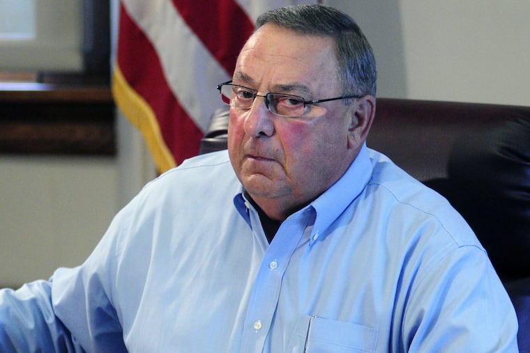Maine Gov. Paul LePage holds up news release with a booking mug shot from a three-ring binder of news releases and articles about drug arrests during a meeting with reporters on Friday, Aug. 26, 2016, in the State House Cabinet room in Augusta, Maine. (Joe Phelan /The Kennebec Journal via AP)